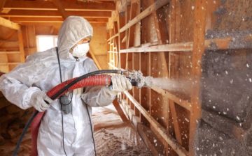 worker installing spray foam insulation in an attic wall