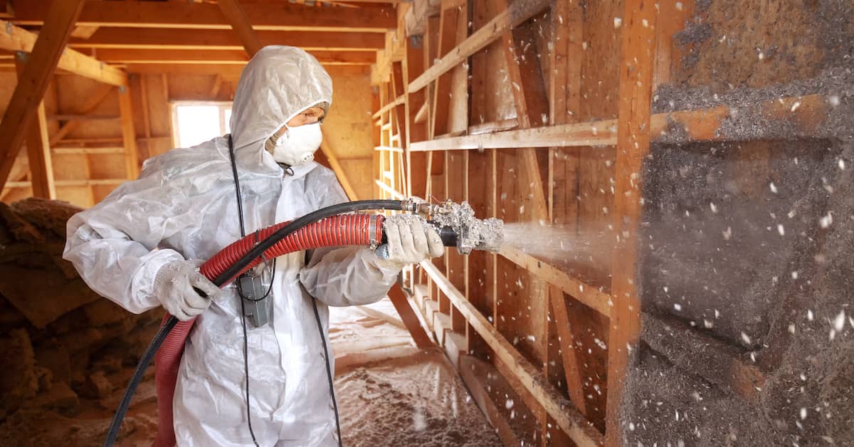 worker installing spray foam insulation in an attic wall
