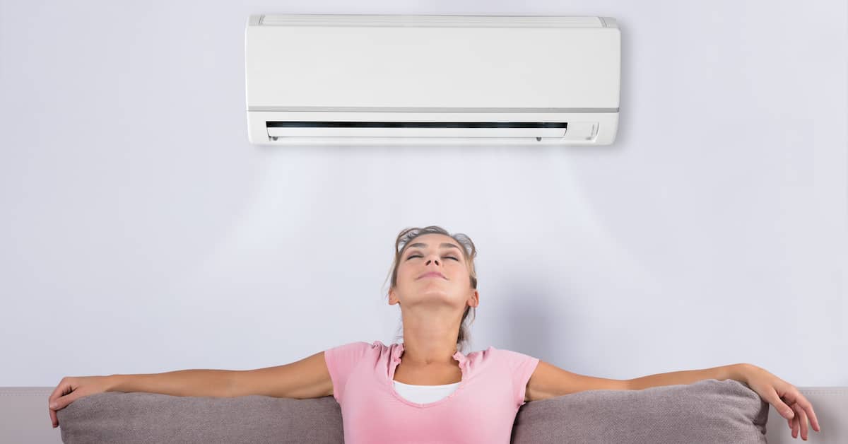 Ductless air conditioner blowing cool air onto young woman | REenergizeCO